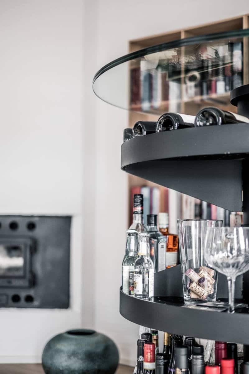 Mat sort metalhylde med flasker, glas og propper.